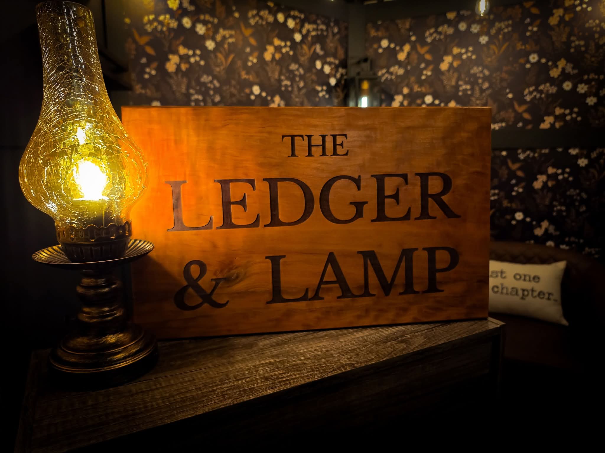 The Ledger & Lamp wooden brand sign illuminated by a vintage oil lamp with cracked-glass shade